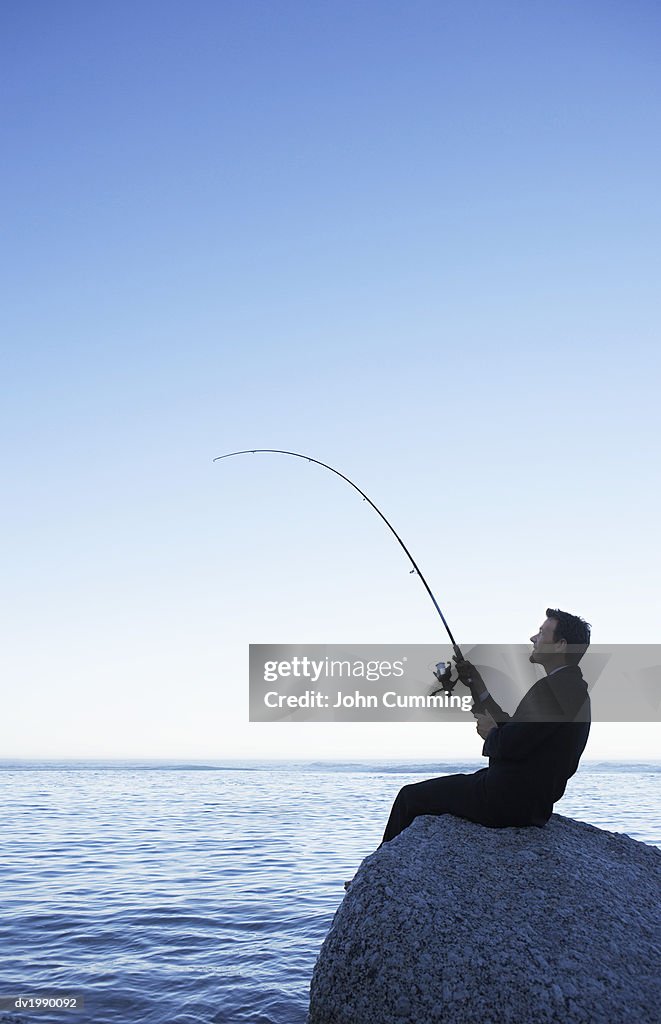 Businessman Fishing from a Rock Against a Blue Sky