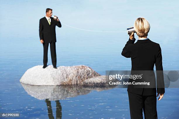 businessman standing on a rock in the sea, talking to a businesswoman through two tin cans connected by string - string - fotografias e filmes do acervo