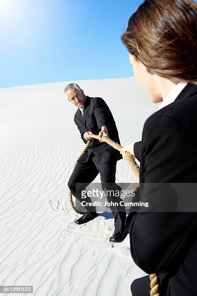 businessman and businesswoman playing tug of war in a desert - war stock-fotos und bilder