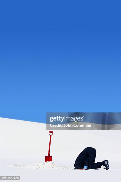 businessman next to a spade hiding his head in a hole in the snow - den kopf in den sand stecken stock-fotos und bilder