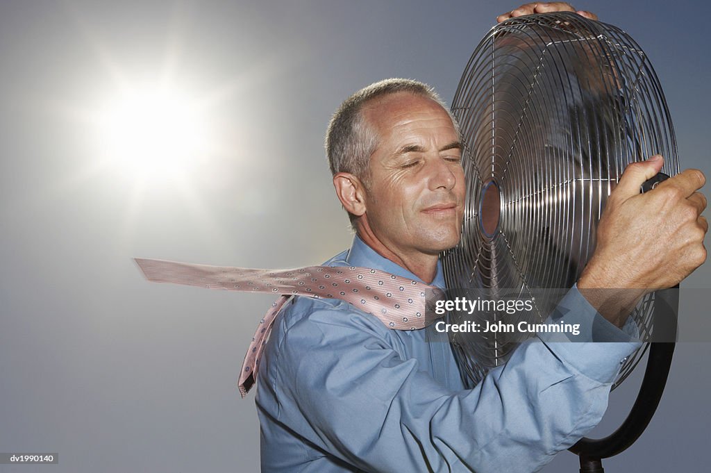 Hot, Relieved Businessman Holding an Electric Fan