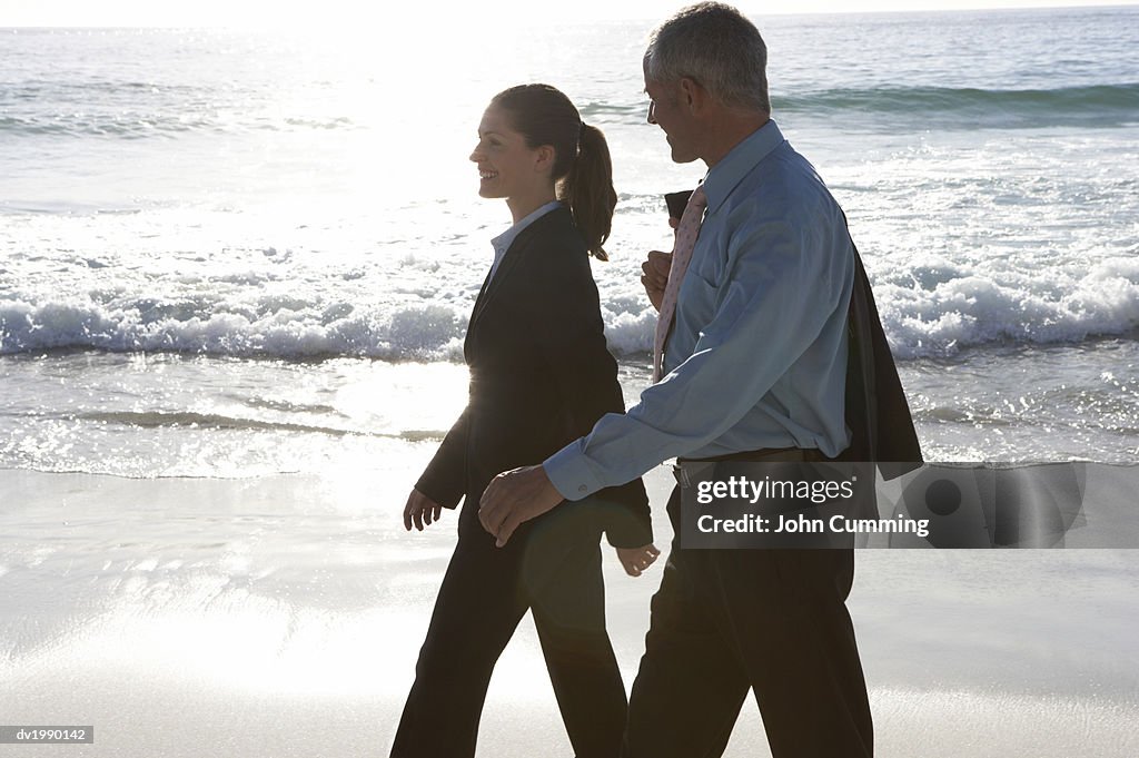 Businessman and a Businesswoman Walking at the Water's Edge on a Beach