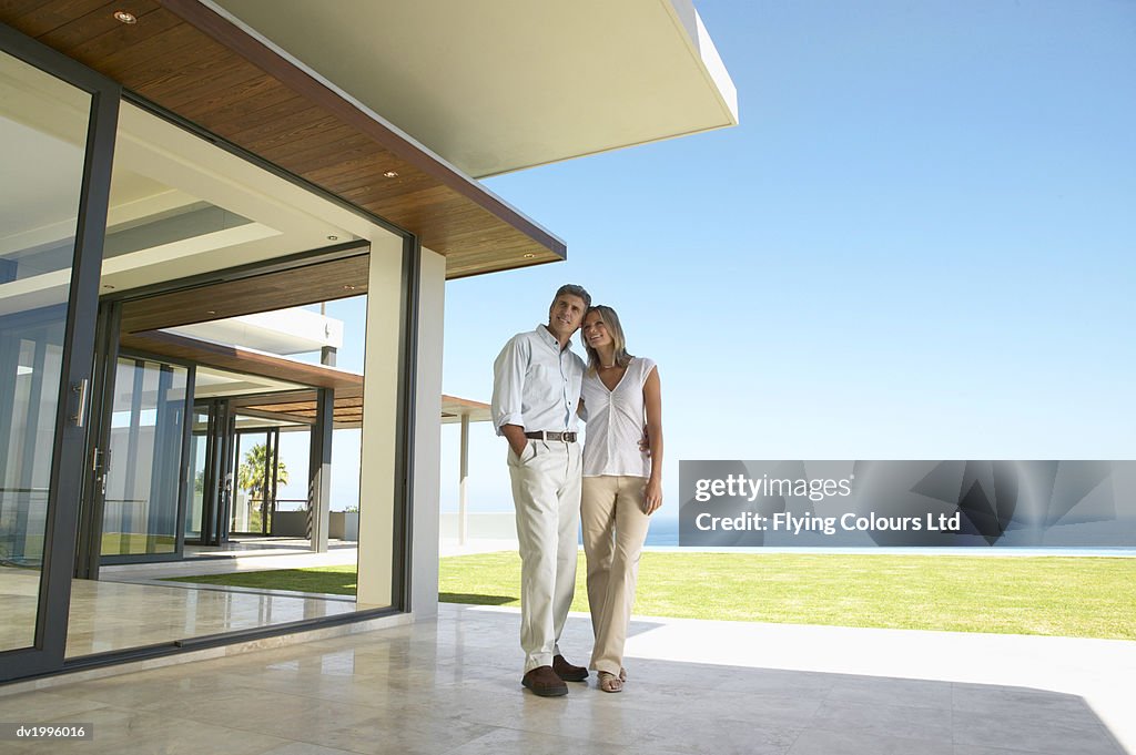 Couple Stand on a Patio Admiring Their Holiday Home by the Sea