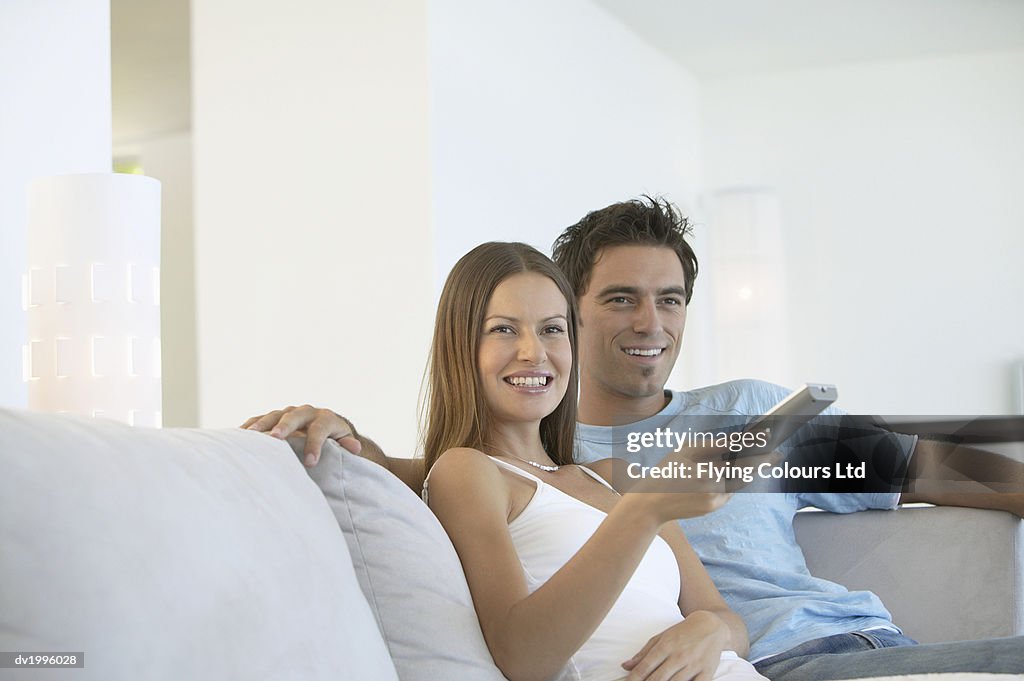 Couple Sitting Side by Side on a Sofa Watching TV and Holding a Remote Control