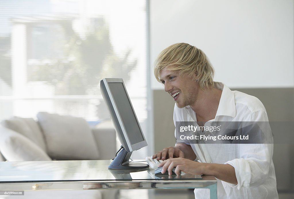 Man Sits at a Glass Table Using His Computer