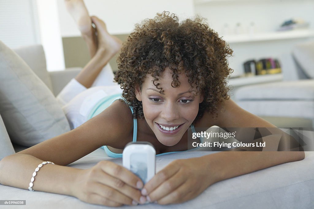 Thirty something Woman Lying on a Sofa Dialing on a Mobile Phone