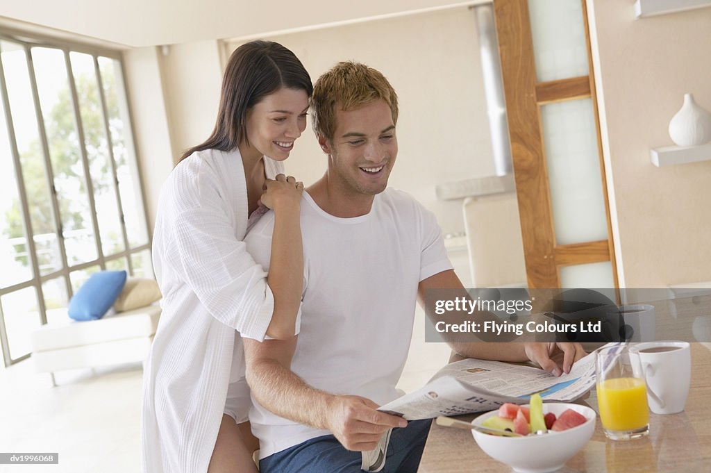 Thirty something Couple Sitting at a Kitchen Counter Reading a Newspaper