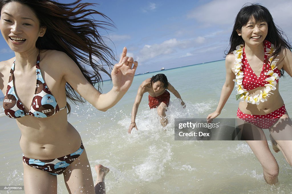 Two Young Women and a Man in Swimwear Run in the Sea, Laughing