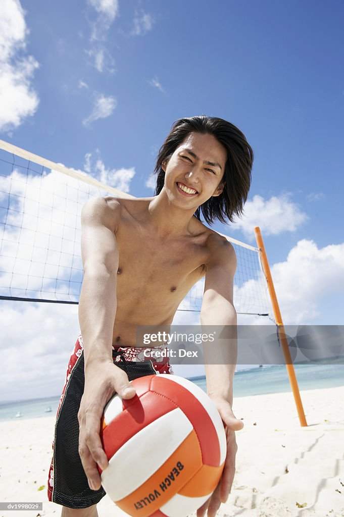 Portrait of a Young Man Standing by a Volleyball Net on the Beach and Holding a Ball