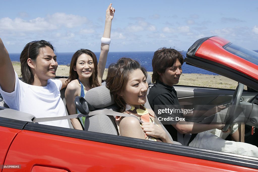 Two Young Couples Sit in a Convertible, Driving by the Sea