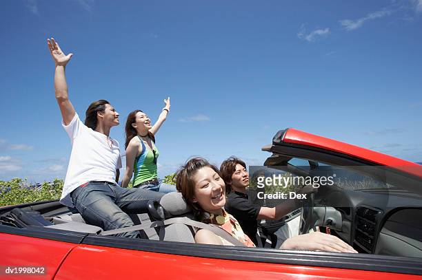 two young couples sit in a convertible, one couple with their arms in the air - fahrspaß stock-fotos und bilder