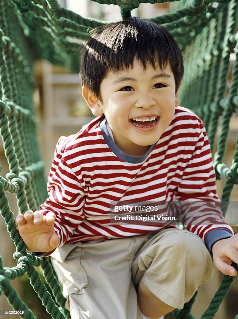 Smiling Young Boy Playing on Climbing Ropes in an Adventure Playground