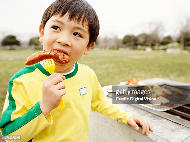 young boy eating a sausage - asian eating hotdog stock-fotos und bilder