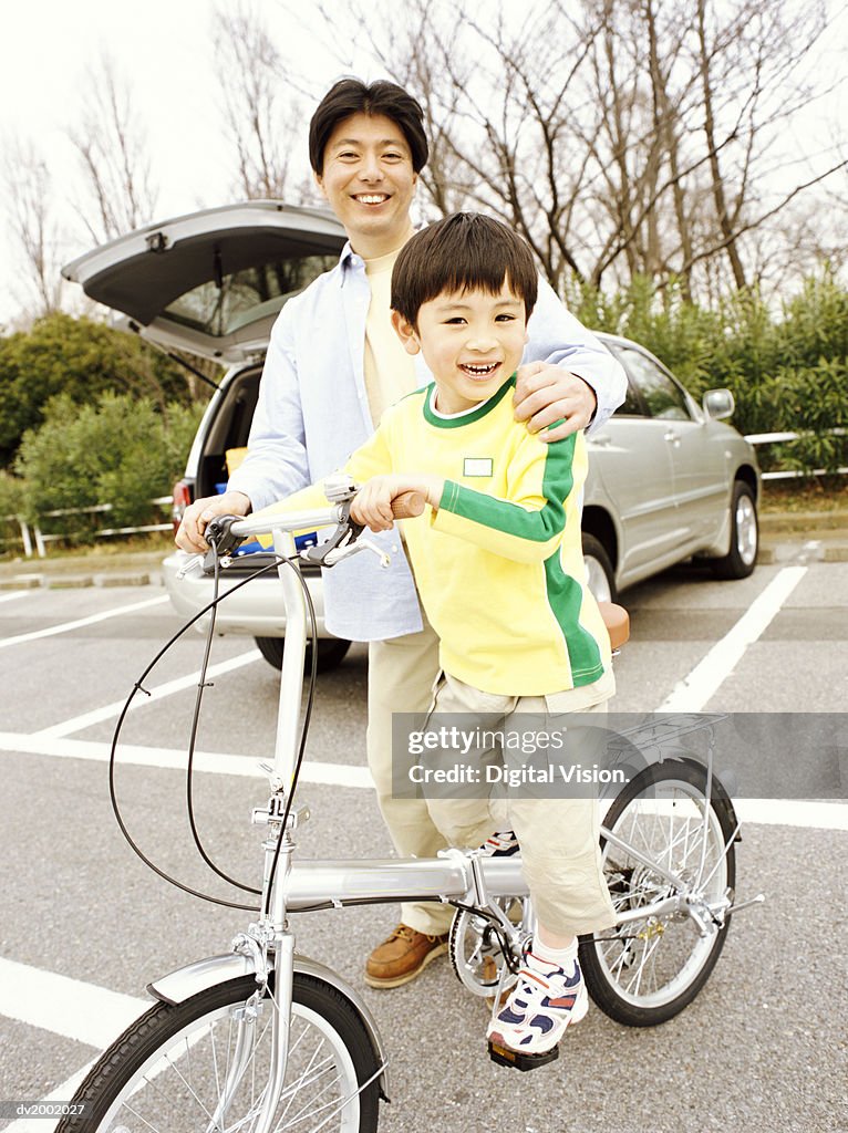 Father Standing with His Arm Around His Son who is Sitting on a Bicycle