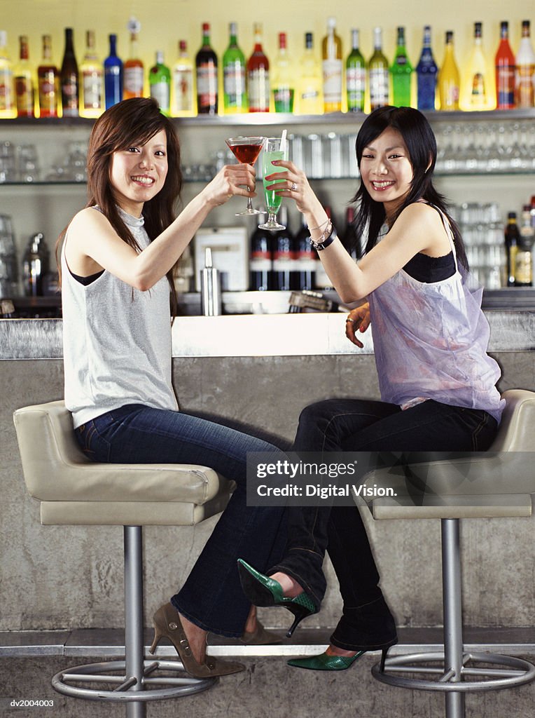 Two Woman Sitting at a Bar Making a Toast With a Cocktail
