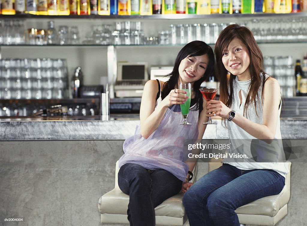 Two Women Sitting at a Bar Making a Toast With Cocktails