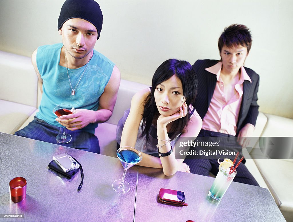 Three Bored Looking People Sitting on a Sofa With Cocktails in Front of Them