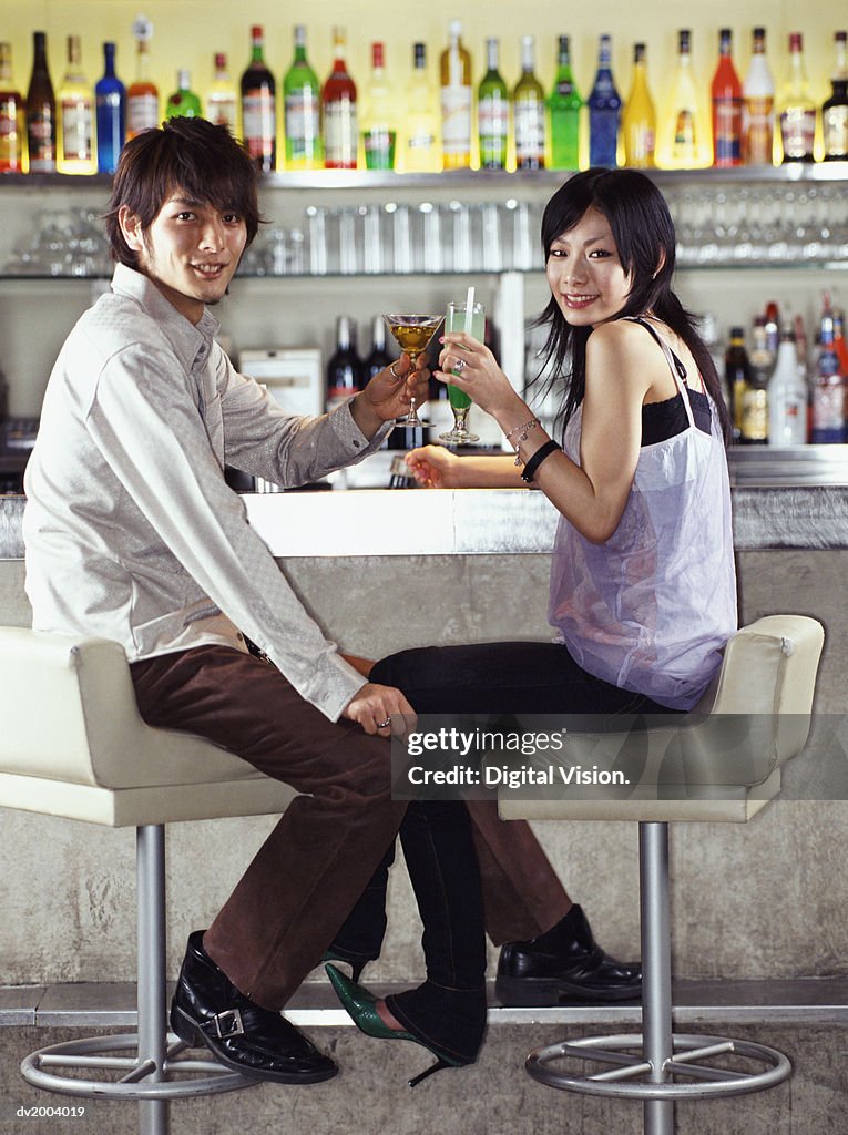 Couple Sitting at a bar Making a Toast With Cocktails