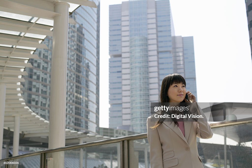 Businesswoman Using a Mobile Phone, with Office Blocks in the Background