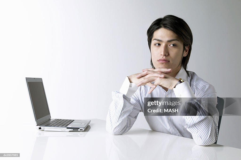 Businessman With His Hands on His Chin Sitting by a Laptop