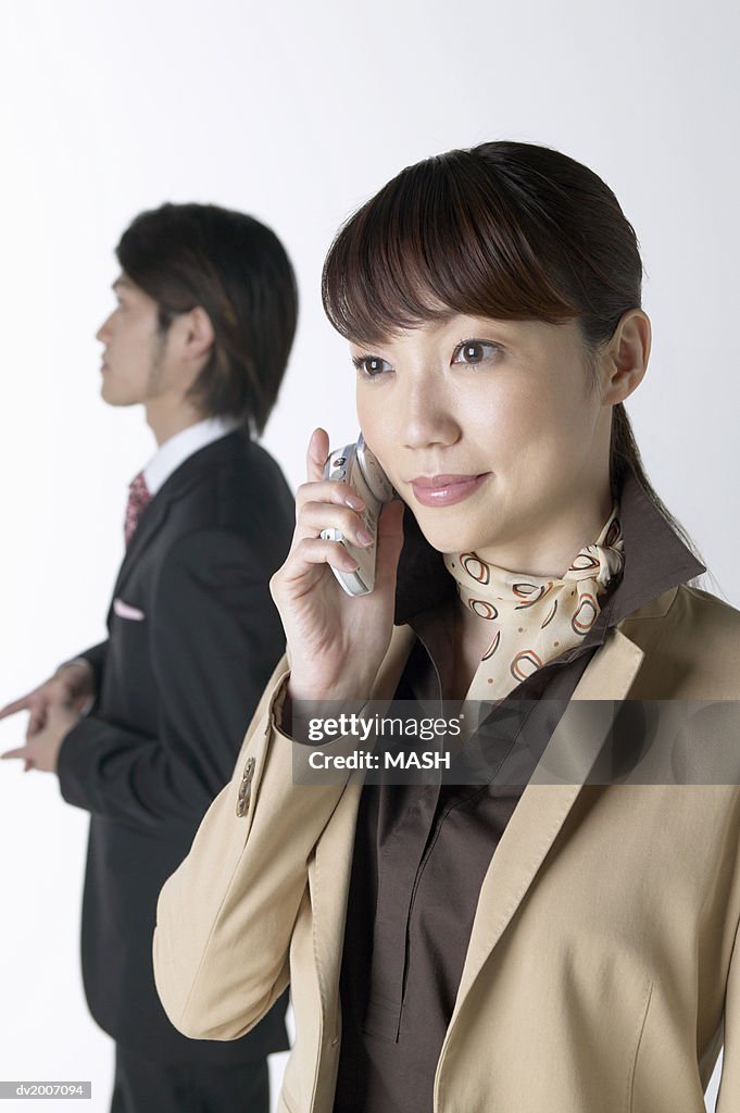 Businesswoman Using a Mobile Phone With a Businessman Standing in the Background