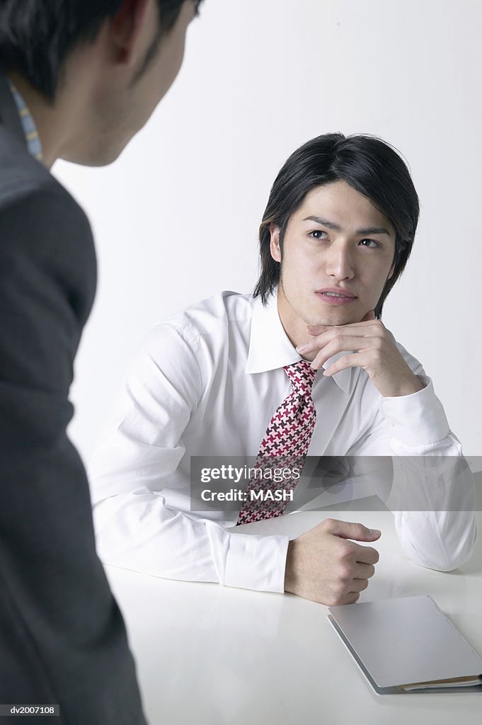 Businessman With His Hand on His Chin Looking at Another Businessman Across a Table