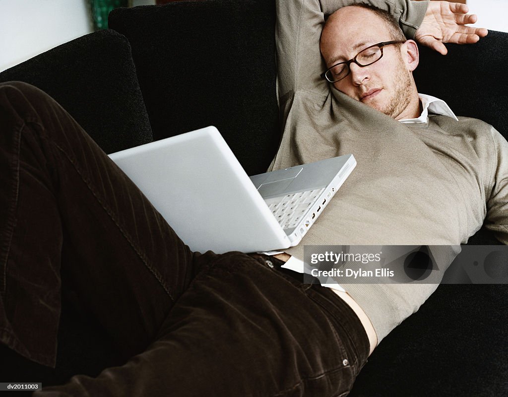 Man Lies on a Sofa, Sleeping, a Laptop on His Lap