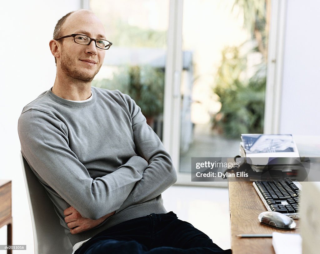 Portrait of a Man Sitting in a Chair By His Desk With His Arms Crossed at Home