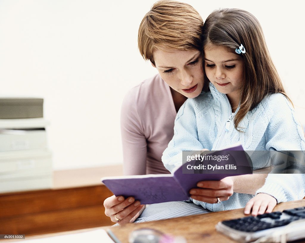 Mother Sits With Her Young Daughter, Reading to Her From a Book