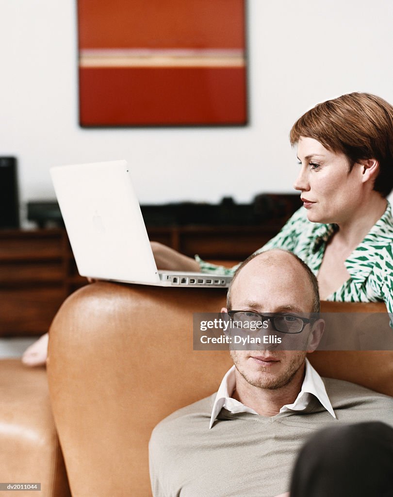 Couple in Their Living Room, Woman Sitting on the Sofa Using a Laptop