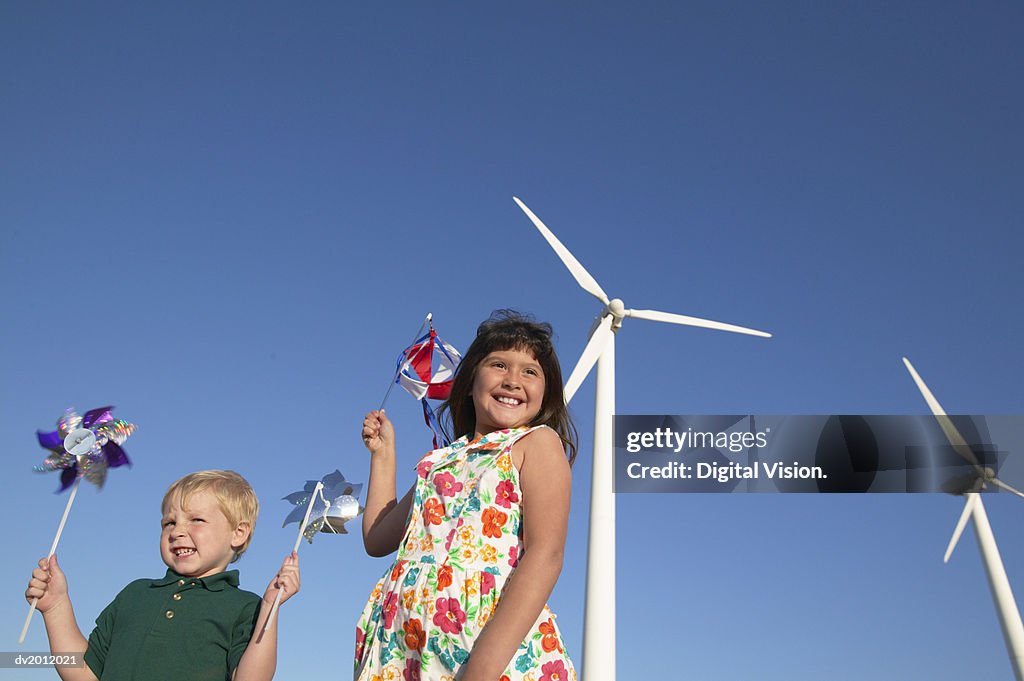 Two Children Holding Pinwheels and Standing in a Wind Farm