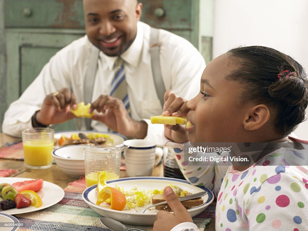 Girl With Her Father at the Breakfast Table Eating a Pineapple