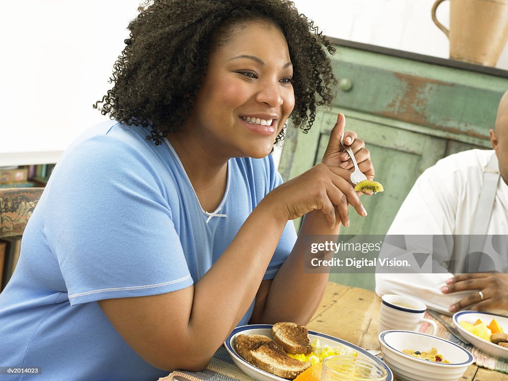 Thirtysomething Woman Eating Fruit at a Table in the Morning