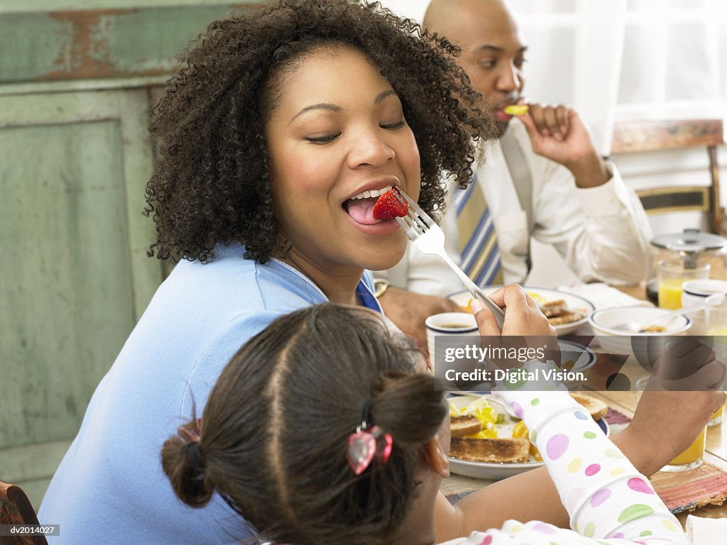 Daughter Feeding Her Mother a Strawberry at Breakfast Father in the Background