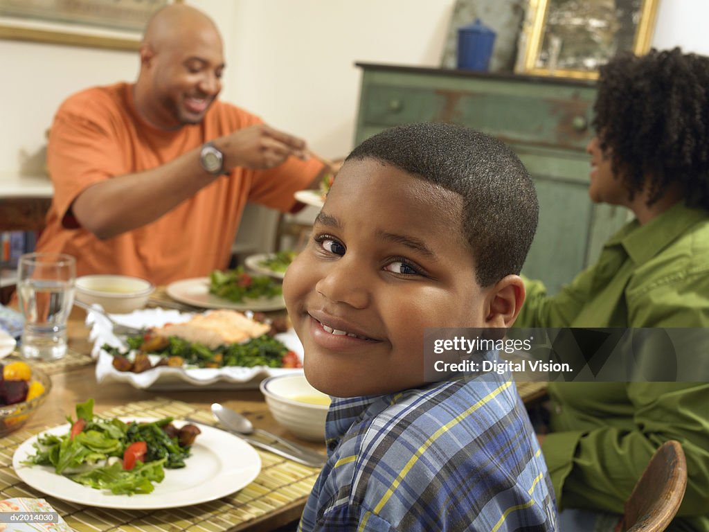 Family Sits at a Table With Food, Boy Looking at Camera