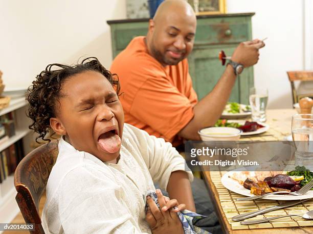 young girl sits at a table for lunch with her father, sticking out her tongue in disgust at the food - girl open mouth stockfoto's en -beelden