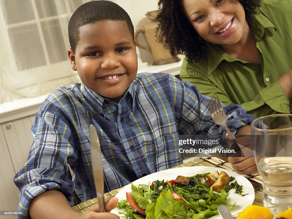 Young Boy Sits at a Table Next to His Mother, With a Plate of Salad