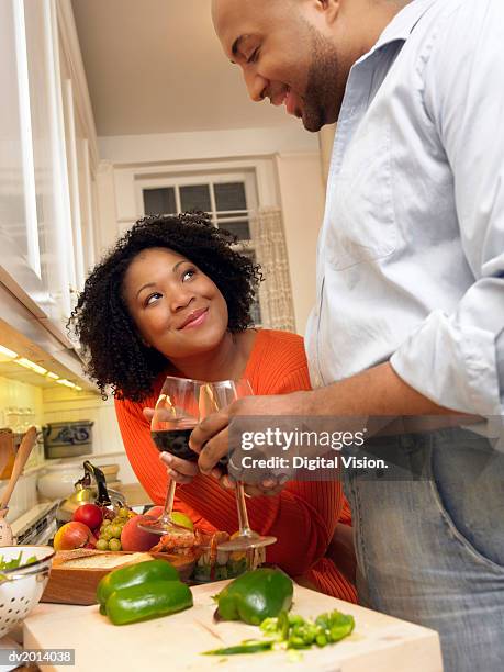 couple stand by a kitchen counter preparing food and making a toast with glasses of red wine - food and wine foto e immagini stock