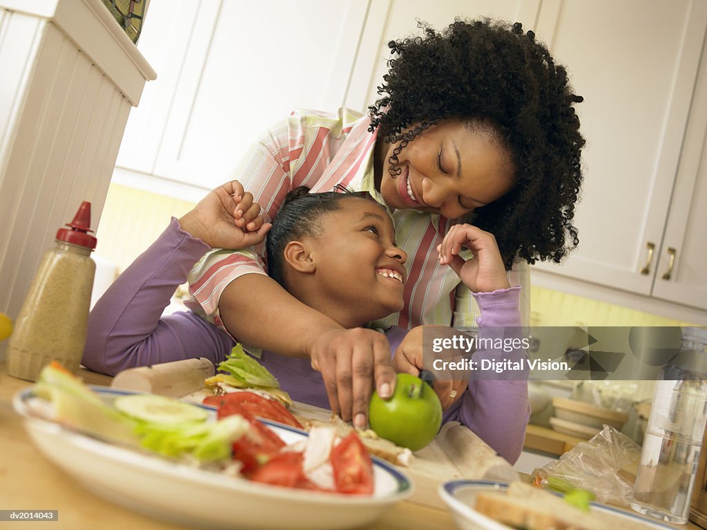 Mother Stands With Her Young Daughter in the Kitchen, Chopping an Apple for Her Lunch