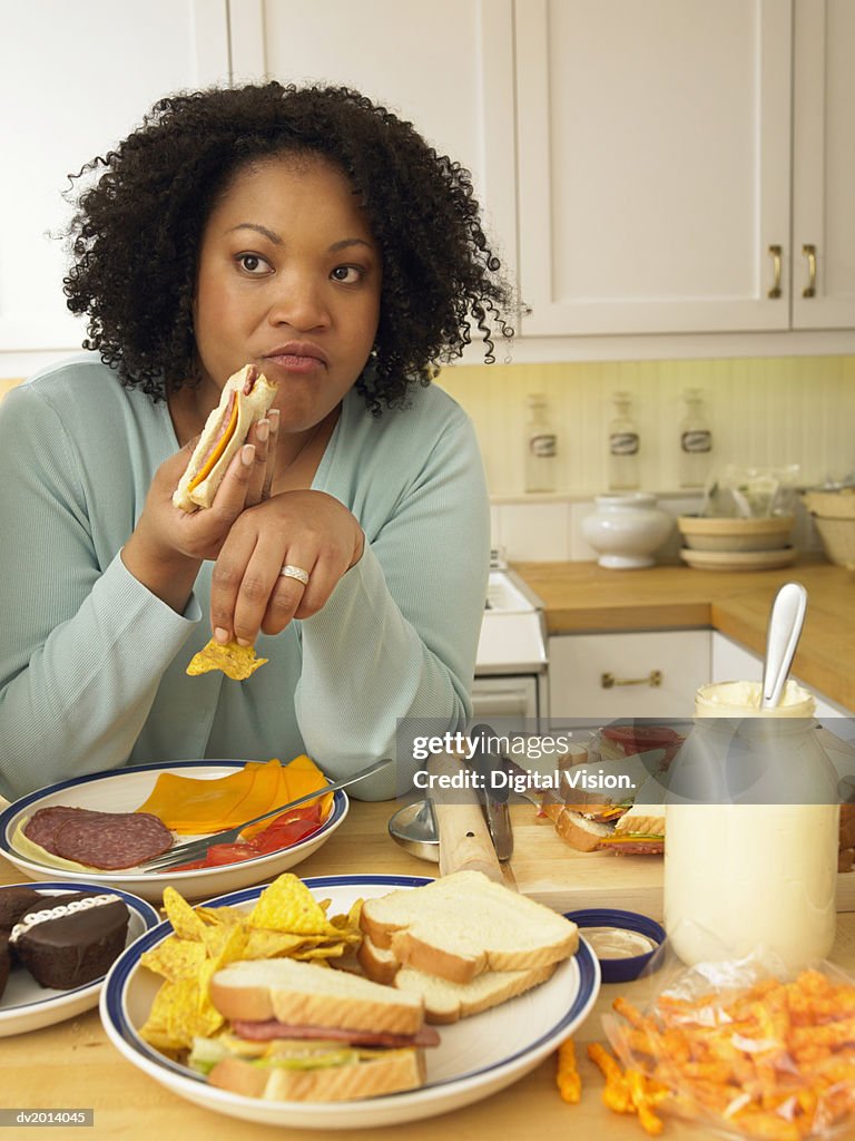 Woman Sits at a Kitchen Table Eating a Lunch of Cheese and Salami Sandwiches and Crisps