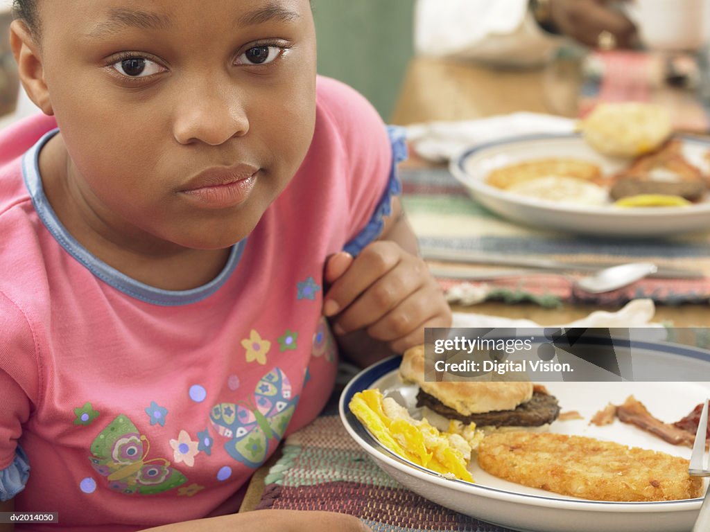 Young Girl Sits at a Table With a Plate of Fried Food for Breakfast, Looking Displeased