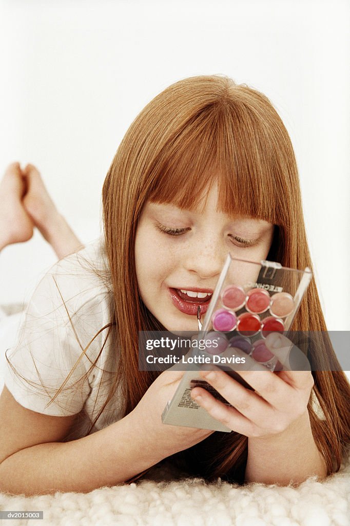 Young Girl Lying on a Bed Applying Lipstick