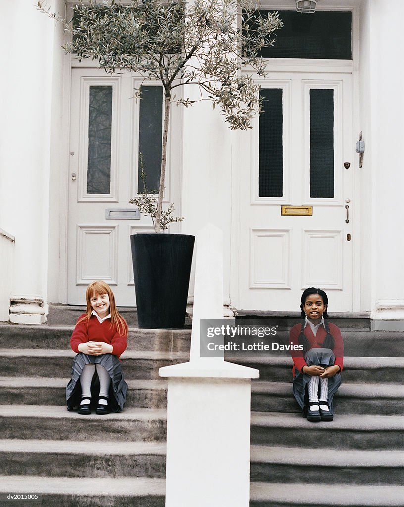 Two Schoolgirls Sitting on Steps In Front of Their Houses