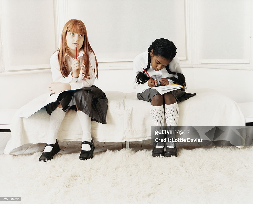 Schoolgirls Doing Their Homework Sitting on a Bed