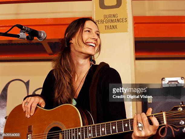 female guitarist stands by a microphone stand on a stage, laughing - woman playing guitar stock pictures, royalty-free photos & images