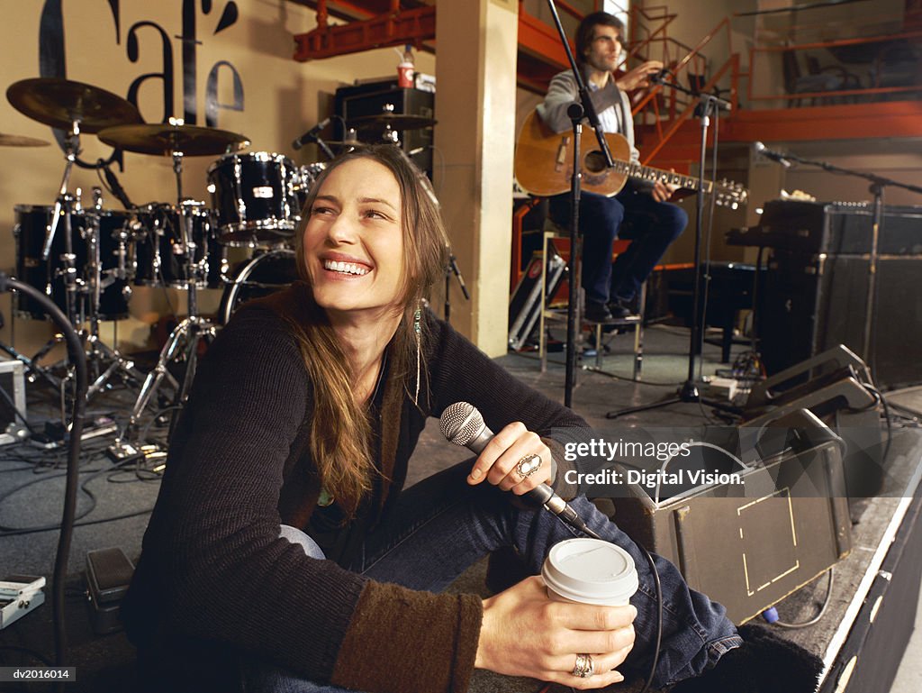 Female Singer Sits on a Stage Having a Coffee Break at a Gig Rehearsal