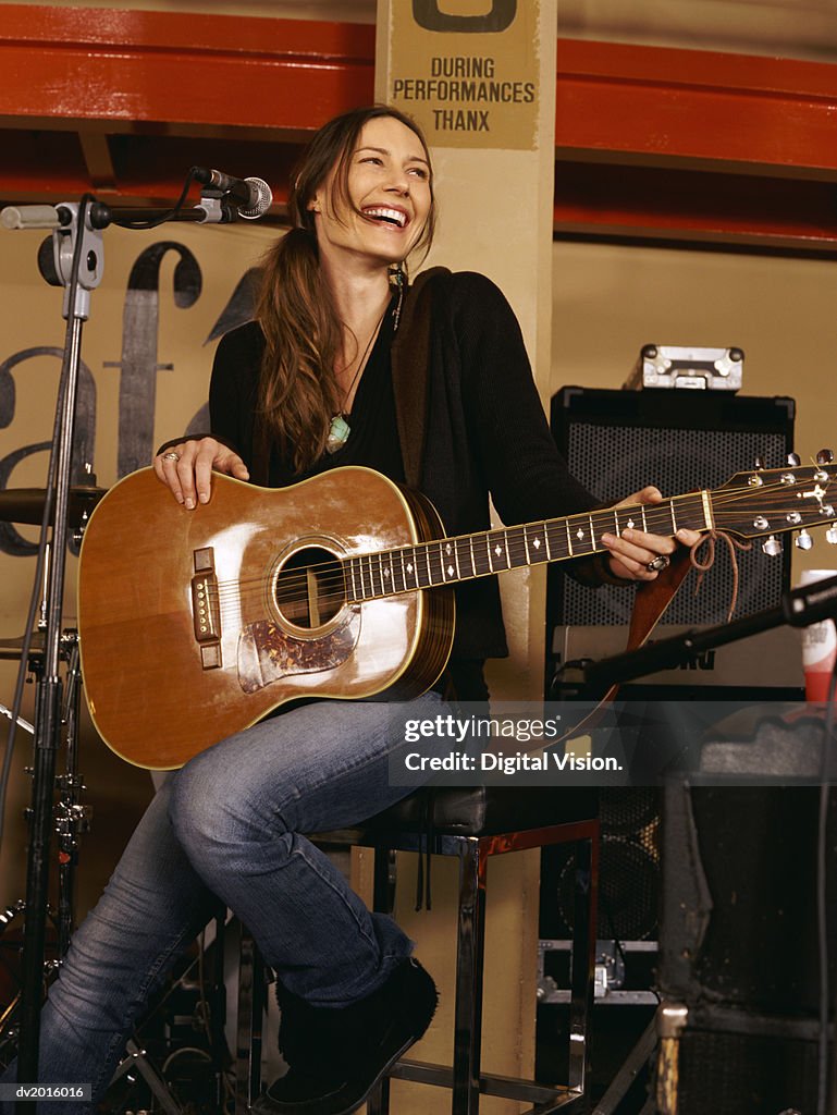 Young Woman Sitting on a Stool and Holding an Acoustic Guitar
