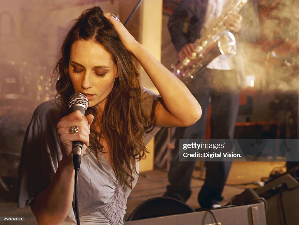 Female Singer Performing on Stage With a Man in the Background Playing a Saxophone