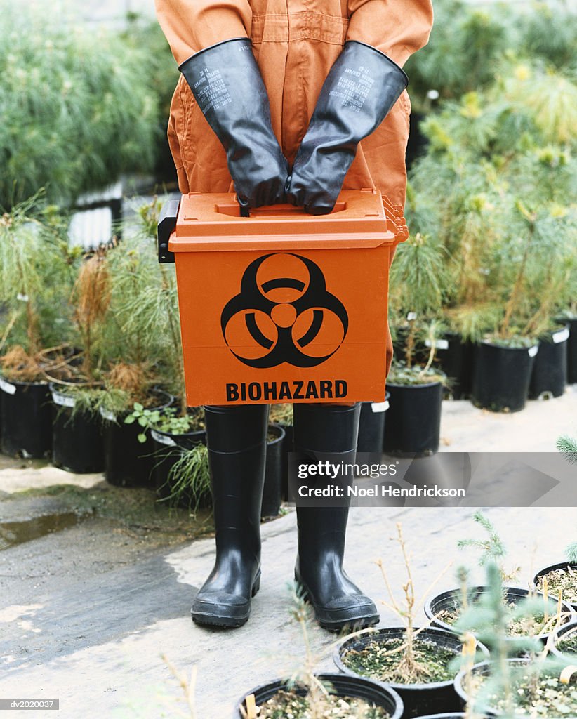 Person Dressed in Protective Clothing Holding a Hazardous Box in a Greenhouse