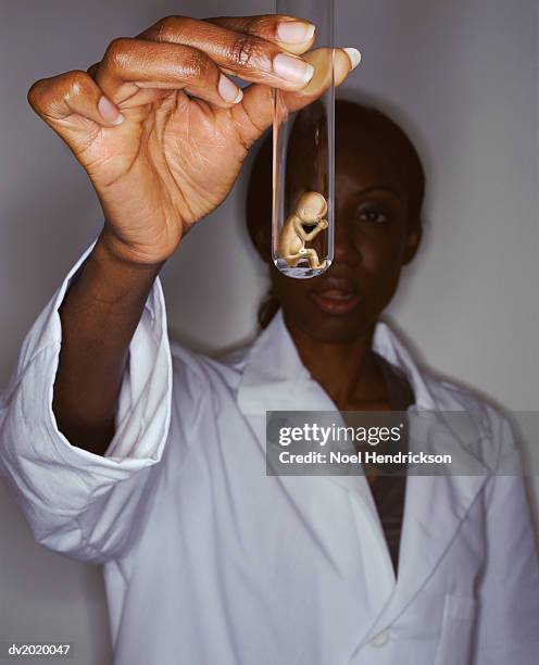 woman in a lab coat holds out a fetus inside a test tube - lab coat stock-fotos und bilder